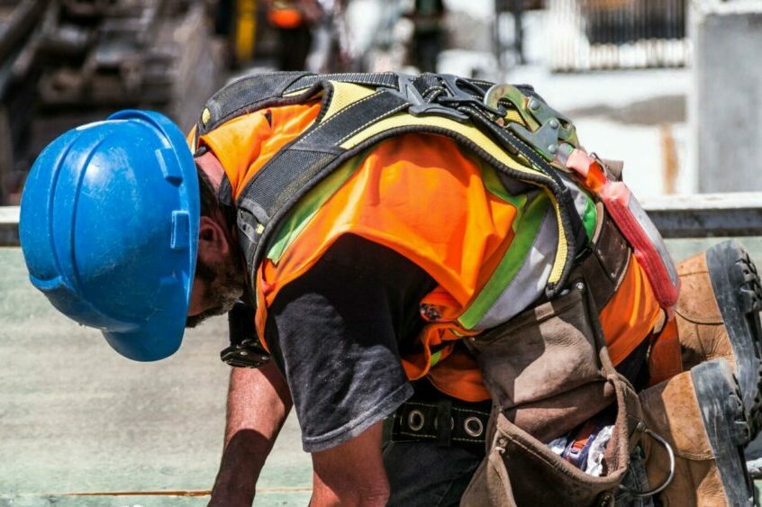 A skilled construction worker in protective gear hammering a rooftop panel.