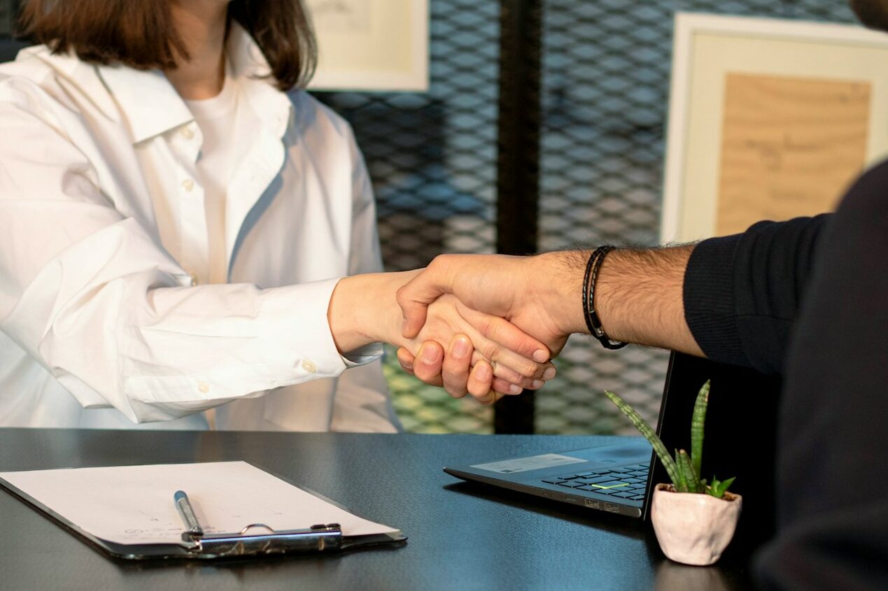 a man and a woman shaking hands in front of a laptop